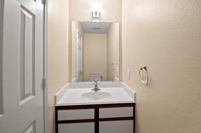bathroom with a textured wall, vanity, and toilet