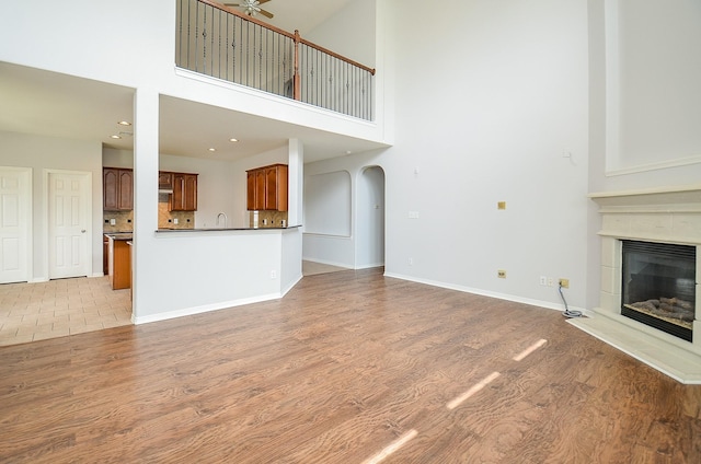 3911 Fallsbrook Ct, Sugar Land, TX 77479 - unfurnished living room with a tiled fireplace, a high ceiling, a ceiling fan, and light wood-type flooring
