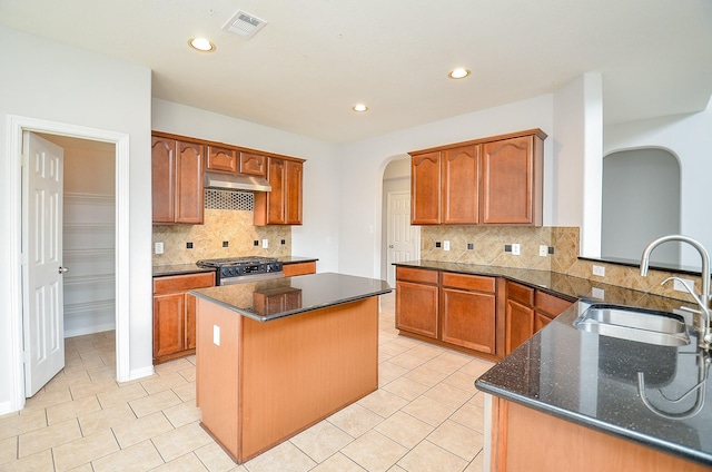 3911 Fallsbrook Ct, Sugar Land, TX 77479 - kitchen featuring a center island, a sink, arched walkways, gas range oven, and under cabinet range hood