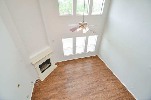 3911 Fallsbrook Ct, Sugar Land, TX 77479 - unfurnished living room featuring baseboards, a glass covered fireplace, a ceiling fan, wood finished floors, and a high ceiling