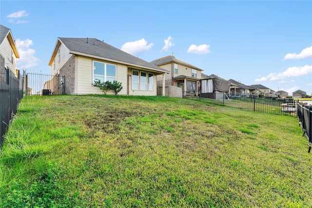 back of property with a fenced backyard, a yard, and central AC
