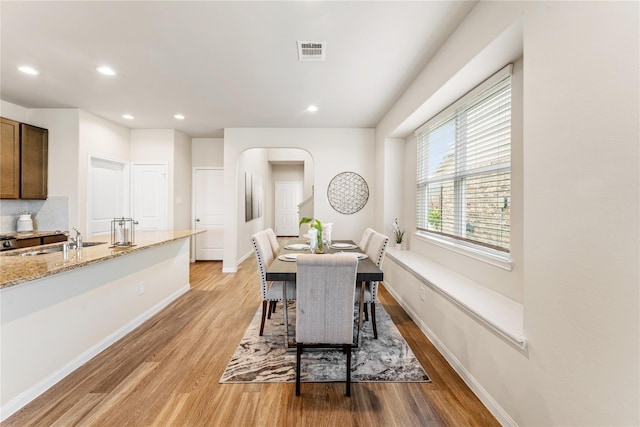 dining area featuring arched walkways, light wood finished floors, baseboards, visible vents, and recessed lighting
