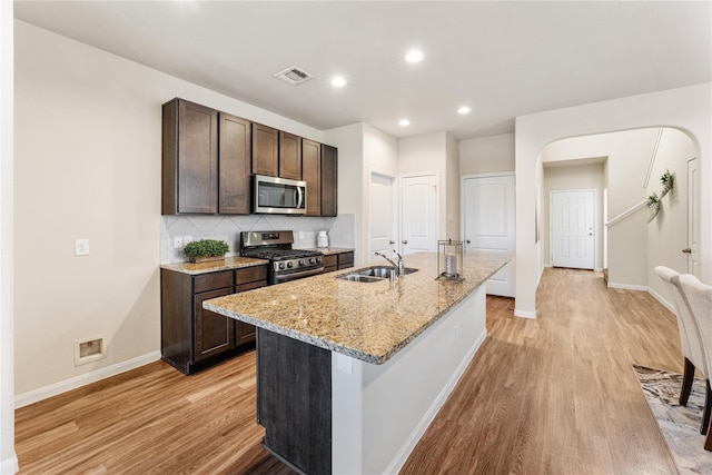 kitchen with stainless steel appliances, dark brown cabinets, a sink, arched walkways, and light wood-type flooring