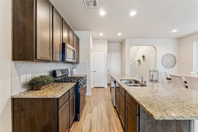 kitchen featuring light wood finished floors, visible vents, a sink, arched walkways, and appliances with stainless steel finishes