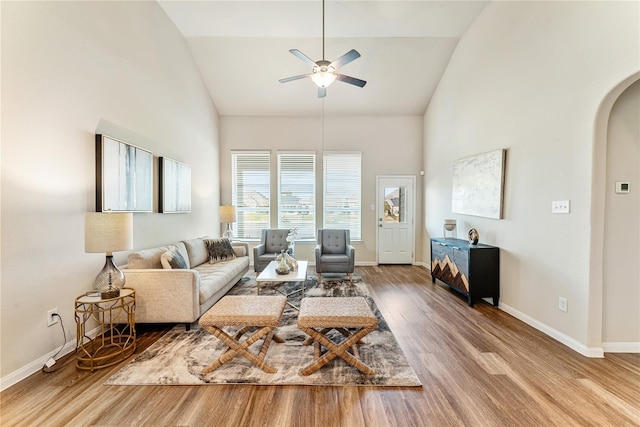 living room featuring arched walkways, baseboards, wood finished floors, ceiling fan, and high vaulted ceiling
