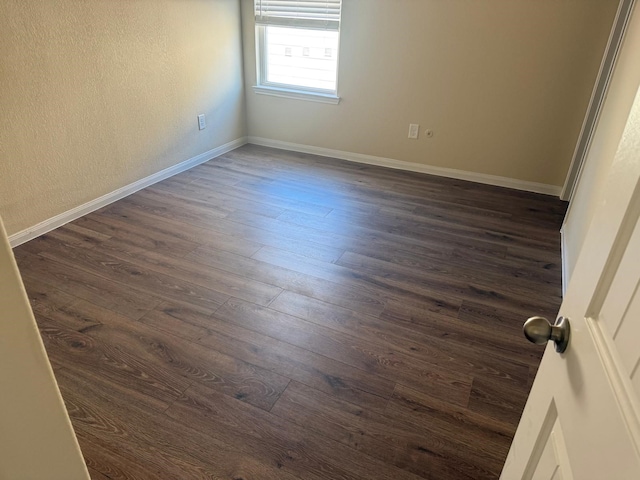 spare room with baseboards and dark wood-style floors