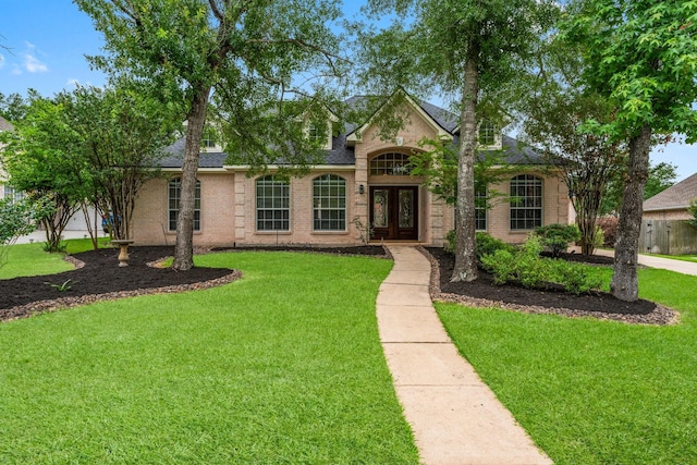view of front of home featuring brick siding, french doors, a front yard, and roof with shingles