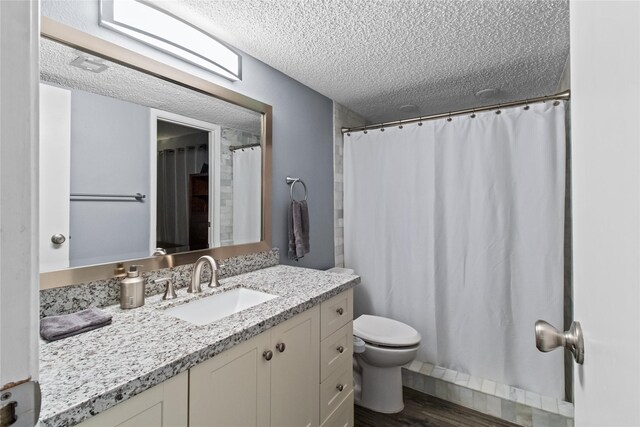 bathroom with toilet, a textured ceiling, wood finished floors, and vanity