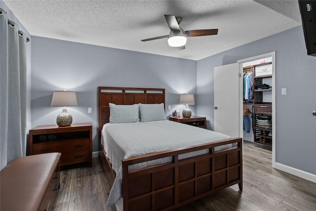 bedroom featuring wood finished floors, a closet, a spacious closet, a ceiling fan, and a textured ceiling
