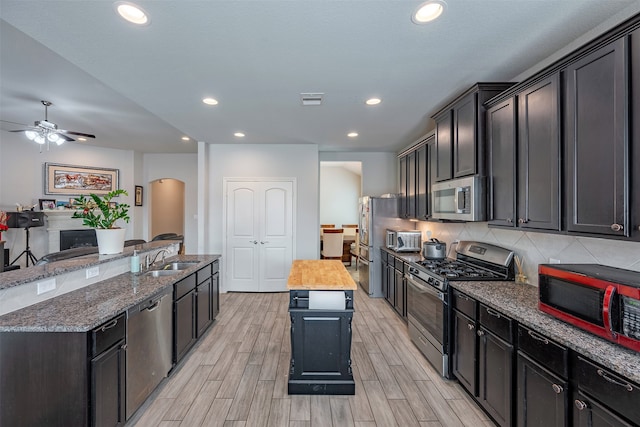 18918 Flintlock Forest Ln, Cypress, TX 77429 - kitchen with stainless steel appliances, a center island with sink, a ceiling fan, light wood-style floors, and backsplash