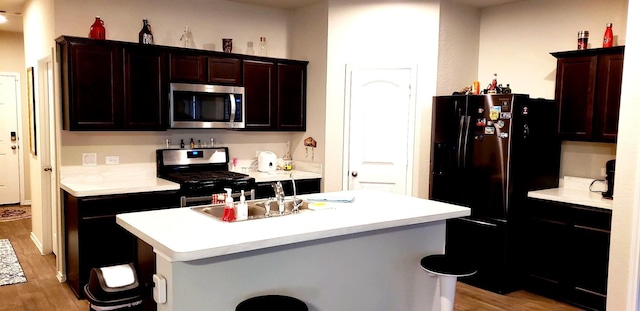 kitchen with a sink, light wood-style floors, a kitchen island with sink, stainless steel appliances, and light countertops