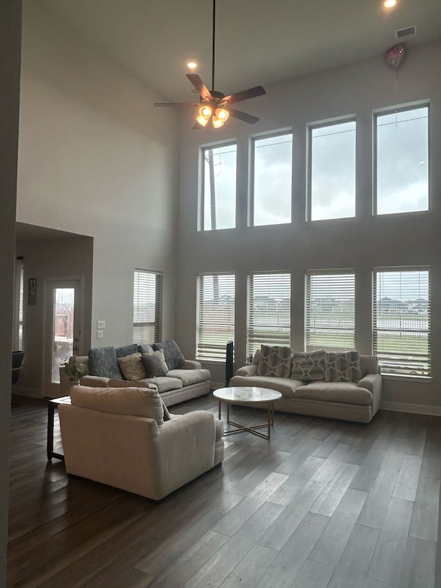 living room with recessed lighting, ceiling fan, dark wood-type flooring, and a towering ceiling