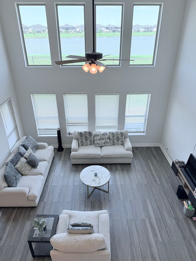 living area with wood finished floors, ceiling fan, a high ceiling, and a water view