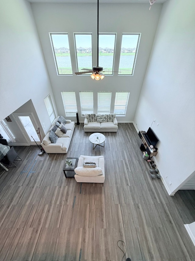 living area with a ceiling fan, baseboards, wood finished floors, a towering ceiling, and a water view
