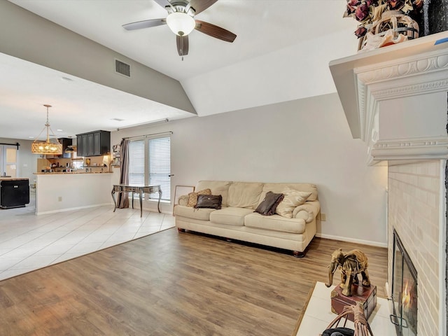 living room featuring ceiling fan with notable chandelier, a tile fireplace, visible vents, and light wood finished floors