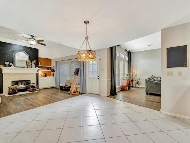 interior space with a tile fireplace, baseboards, ceiling fan, and light tile patterned floors