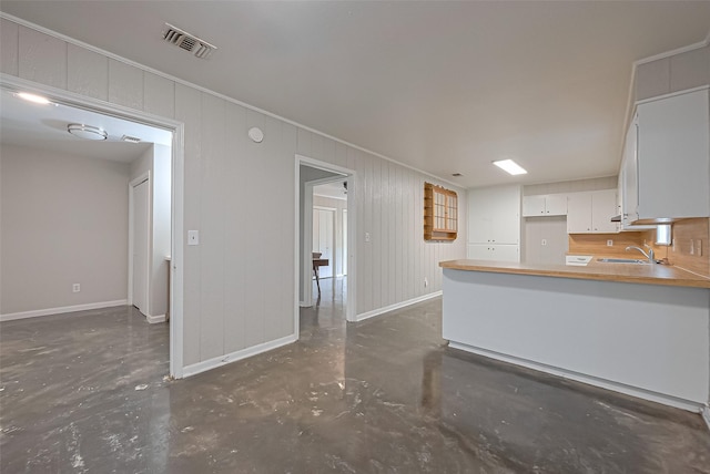 kitchen featuring white cabinets, visible vents, concrete flooring, crown molding, and baseboards