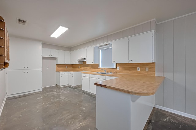 kitchen with a peninsula, a sink, visible vents, concrete floors, and under cabinet range hood
