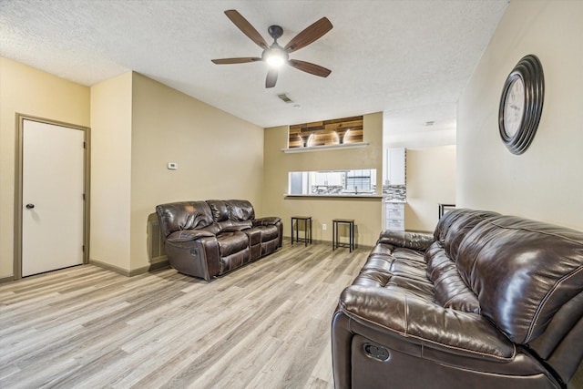 living area featuring light wood-style floors, baseboards, visible vents, a ceiling fan, and a textured ceiling