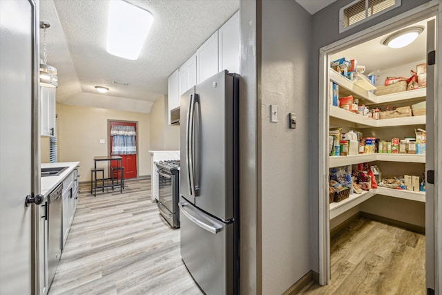 kitchen with stainless steel appliances, light countertops, white cabinetry, light wood-type flooring, and a textured ceiling