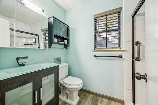 bathroom with vanity, toilet, a stall shower, baseboards, and wood finished floors