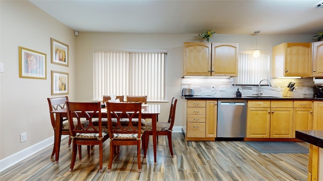 kitchen featuring dark countertops, stainless steel dishwasher, a sink, and light wood-style flooring