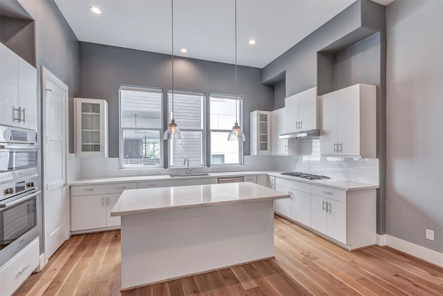 kitchen featuring tasteful backsplash, stainless steel appliances, light wood-style floors, light countertops, and a sink