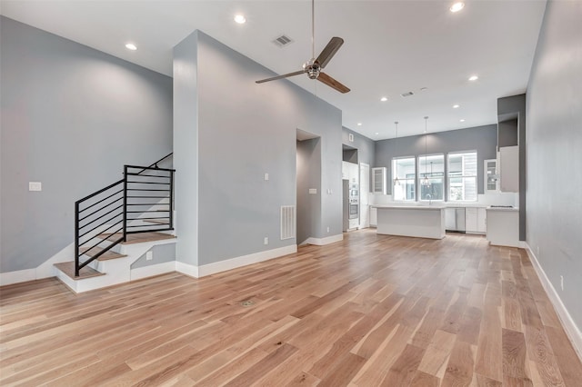 unfurnished living room with stairway, visible vents, a ceiling fan, and light wood-style flooring