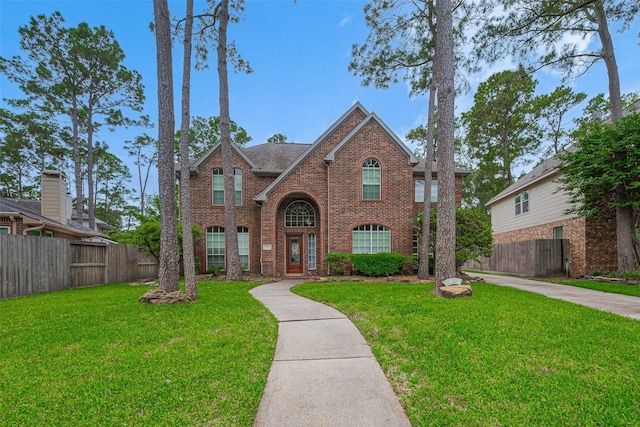 traditional home with brick siding, a shingled roof, fence, and a front yard