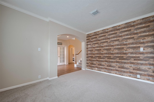 spare room featuring crown molding, arched walkways, wood walls, baseboards, and visible vents