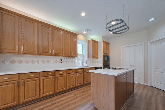 kitchen with wood finished floors, brown cabinets, tasteful backsplash, a sink, and black appliances