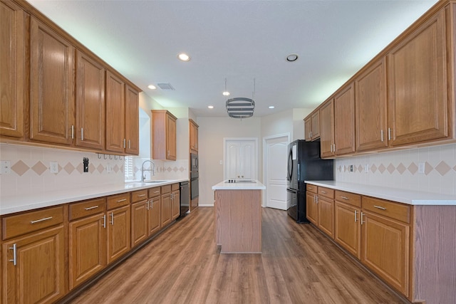 kitchen with wood finished floors, a kitchen island, brown cabinets, a sink, and black appliances