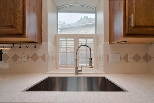 room details with light stone counters, brown cabinetry, a sink, and tasteful backsplash