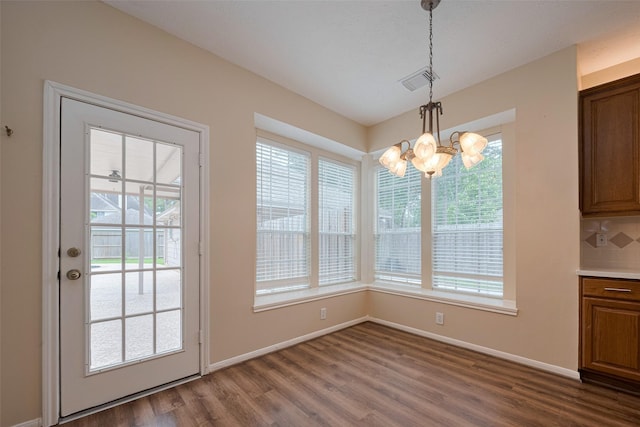 unfurnished dining area with baseboards, a notable chandelier, dark wood-style floors, and a wealth of natural light