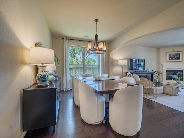 2560 Wild Oak Forest Ln, Seabrook, TX 77586 - dining space with arched walkways, a glass covered fireplace, an inviting chandelier, and dark wood-type flooring