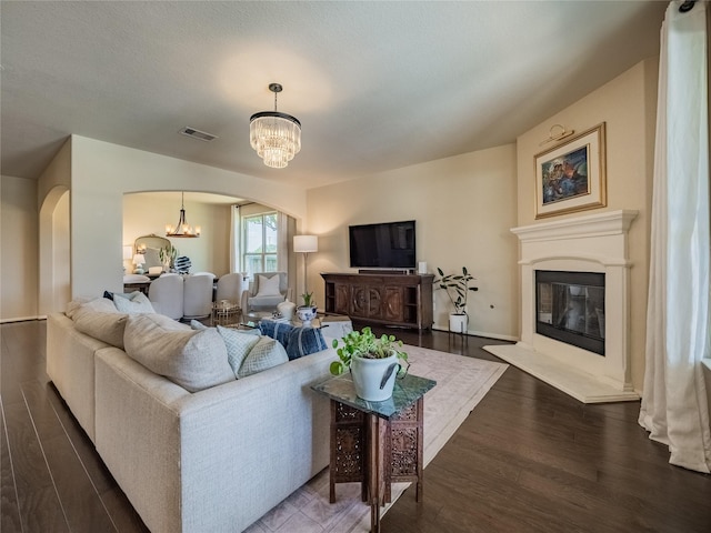2560 Wild Oak Forest Ln, Seabrook, TX 77586 - living room featuring a notable chandelier, dark wood finished floors, visible vents, arched walkways, and a glass covered fireplace