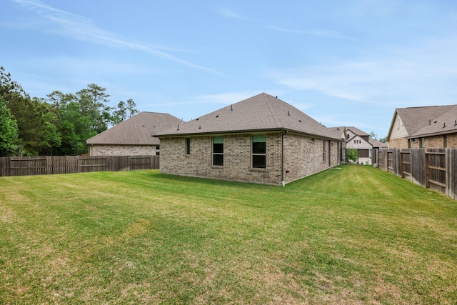 rear view of house with a fenced backyard, a lawn, roof with shingles, and brick siding