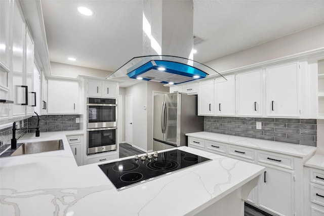 kitchen with stainless steel appliances, a sink, white cabinetry, island range hood, and decorative backsplash