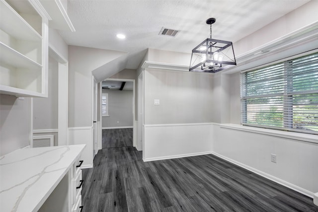 unfurnished dining area featuring dark wood finished floors, visible vents, wainscoting, a chandelier, and a textured ceiling