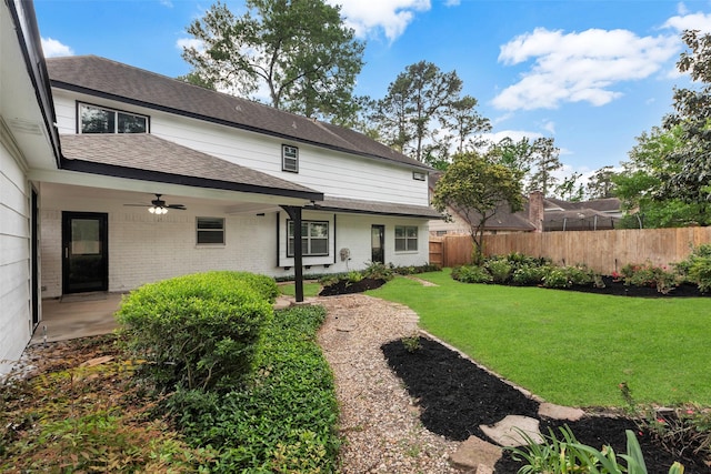 rear view of property featuring a patio area, a lawn, fence, roof with shingles, and ceiling fan