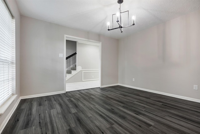 unfurnished room featuring stairs, baseboards, an inviting chandelier, and dark wood-type flooring