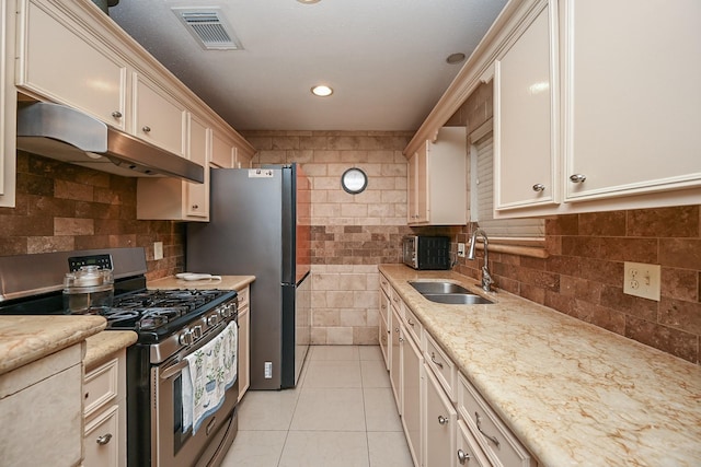 kitchen with a sink, light tile patterned floors, appliances with stainless steel finishes, under cabinet range hood, and visible vents