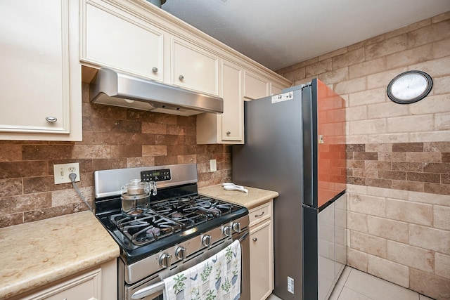 kitchen featuring under cabinet range hood, light tile patterned flooring, light countertops, and stainless steel gas stove