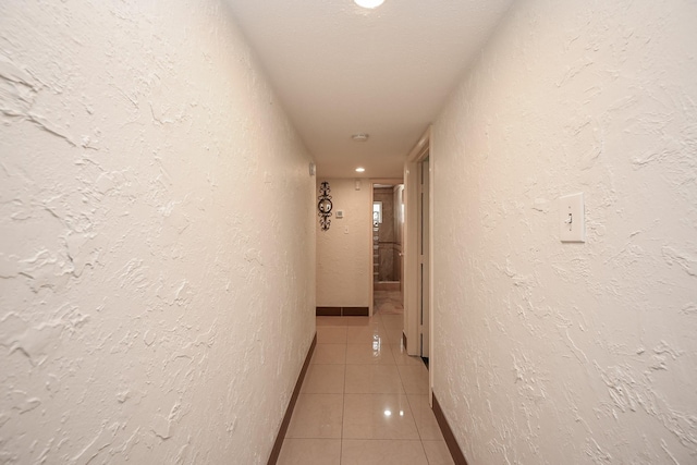 hall with a textured wall, baseboards, and light tile patterned floors
