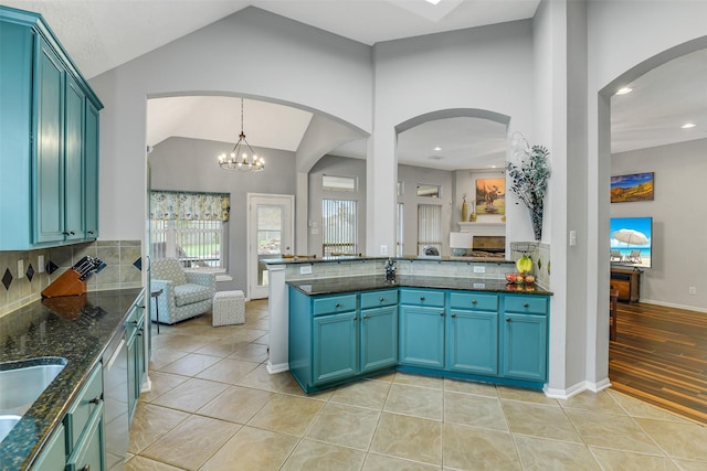 kitchen with lofted ceiling, dark stone countertops, stainless steel dishwasher, light tile patterned floors, and tasteful backsplash