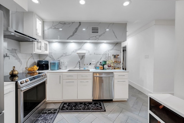kitchen featuring a sink, stainless steel appliances, wall chimney exhaust hood, white cabinetry, and visible vents