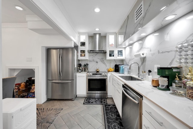 kitchen featuring white cabinets, stainless steel appliances, a sink, glass insert cabinets, and wall chimney range hood