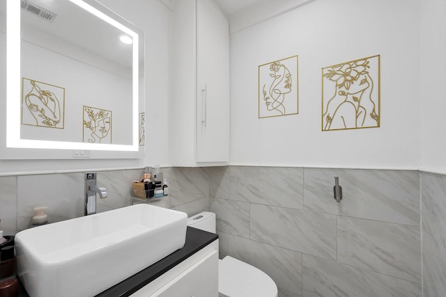 half bath featuring toilet, vanity, visible vents, and tile walls