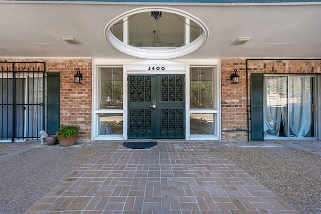 doorway to property with covered porch, brick siding, and visible vents