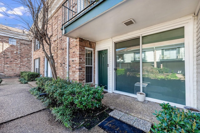 view of exterior entry featuring brick siding and a balcony
